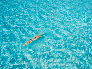 Woman swimming in clear blue sea on sunny day. Drone view