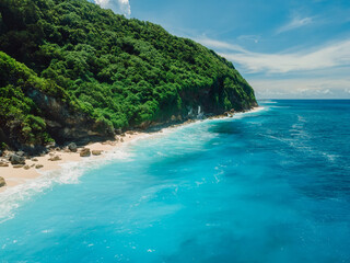 Fototapeta premium Aerial view of coastline with turquoise ocean and tropical beach under rocky cliffs.