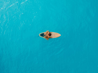 Surf girl sitting on surfboard in blue ocean. Aerial view