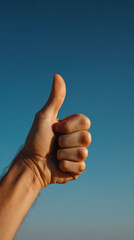 Thumbs up hand gesture close up against clear blue sky, positive and encouraging mood