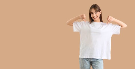 Young woman pointing at her white t-shirt on beige background with space for text