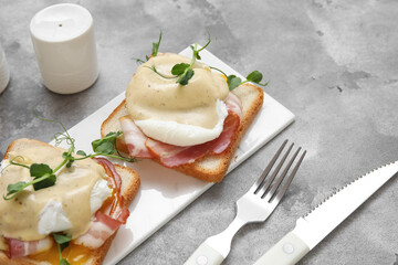 Board with tasty eggs Benedict and cutlery on grey grunge background