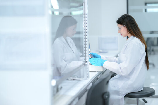 A pharmaceutical technician performs aseptic compounding inside a sterile biosafety cabinet, preparing a cell culture for biologic drug development under strict quality control conditions.