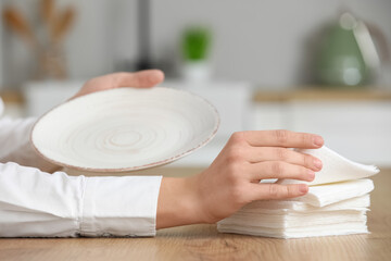 Woman with stack of paper napkins and plate at table in kitchen