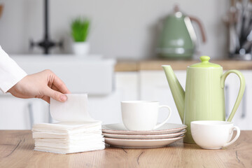 Woman with stack of paper napkins, plates, cups and teapot at table in kitchen