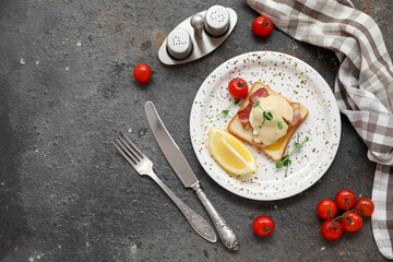Plate of delicious egg Benedict with bacon and lemon on dark background