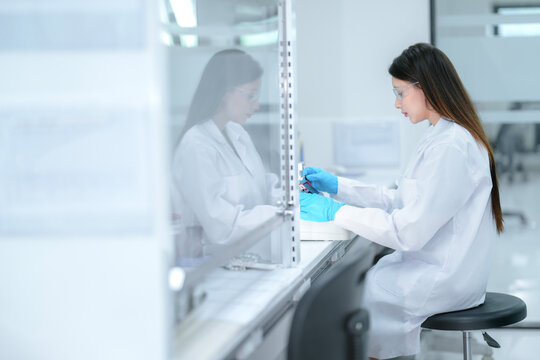 A pharmaceutical technician performs aseptic compounding inside a sterile biosafety cabinet, preparing a cell culture for biologic drug development under strict quality control conditions. - Powered by Adobe