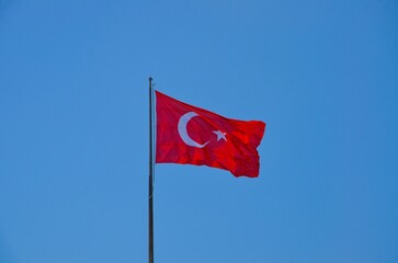 The Turkish flag flutters in the wind against a blue sky
