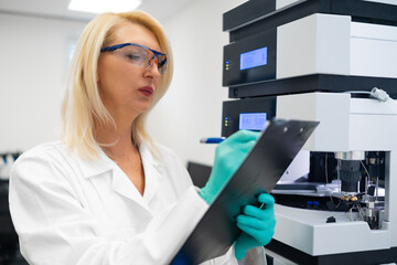 Professional blonde scientist writing a report on HPLC data. Pharmaceutical science and testing.