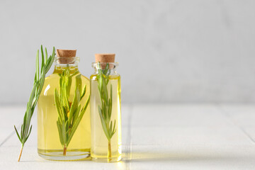 Fresh rosemary with bottles of essential oil on light background