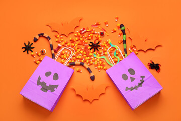 Shopping bags, paper bats and tasty candies for Halloween on orange background