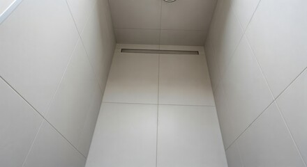 Upward view into a bright, minimalist interior corner featuring light grey square tiles on walls and ceiling, with a subtle linear vent.