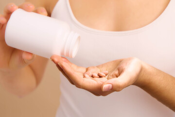 Asian woman pours pills from a bottle into her hand in a calm domestic setting, illustrating health awareness and personal care as part of everyday wellness.