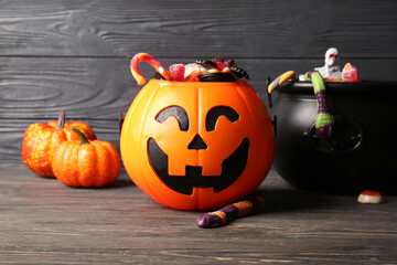Decorative pumpkin and cauldron with different sweet candies on black wooden background. Halloween...