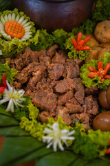 Close-up of spicy braised beef chunks (sambal goreng daging) served on a banana leaf with lettuce and carved vegetable garnishes
