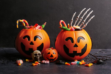 Decorative pumpkins with different sweet candies and skeleton hand on dark background. Halloween celebration