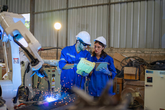 Blue collar workers at machine shop with welding robot arm.