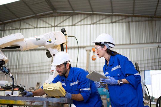 Blue collar workers at machine shop with welding robot arm. - Powered by Adobe