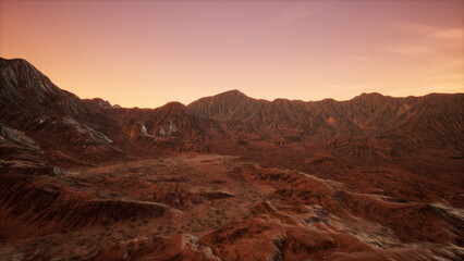 Golden hues illuminate the rugged mountain peaks as the sun sets in the vast desert. Rocks and dry vegetation create an otherworldly atmosphere, showcasing natures striking beauty.