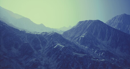 A vast mountain landscape features towering peaks and rugged terrain bathed in soft blue light during twilight. Shadows stretch across the rocky surfaces, creating depth.