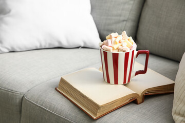 Cup of cocoa with book on sofa in living room, closeup. Christmas celebration