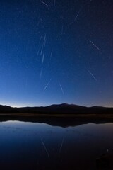 meteor. Vibrant meteor trails painting the night sky, mirrored perfectly in a tranquil alpine lake. travel magazines, destination branding, designed for outdoor magazines and nature guides.
