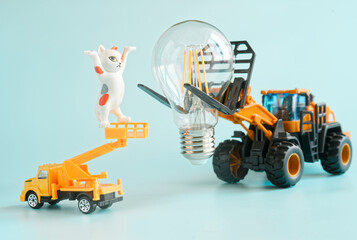 Toy forklift and cute kitten figurine install an LED light bulb on blue background, symbolizing electric work, learning and energy saving. Photo