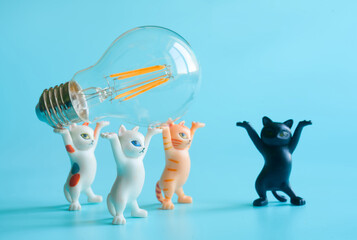 Funny toy kittens lifting an LED light bulb together on a blue background, symbolizing teamwork, learning, and energy saving. Photo