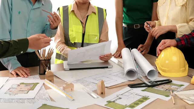 Smart architect and safety engineer discussion about building blueprint on table with architectural document, measurement tools and wooden block scatter around at modern office. Closeup. Delineation.