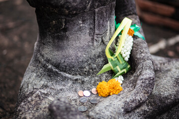 Floral patterns and coins religious offerings on a stone buddha sculpture in Ayutthaya, Thailand
