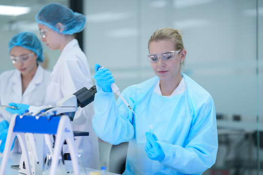 A senior scientist mentors a junior researcher, pointing at results on a digital tablet as they collaborate on an experiment in a bustling, modern scientific laboratory environment.