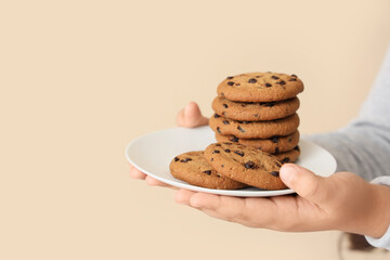 Little girl's hands with tasty cookies on beige background, closeup