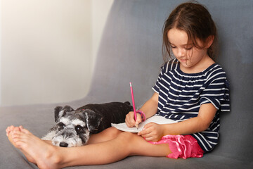 Child drawing  while sitting on sofa with dog