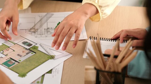 Architects using measurement tool and pencil tracing in building blueprint by coworker support on table with architectural document and wooden block scatter around at office. Closeup. Delineation.