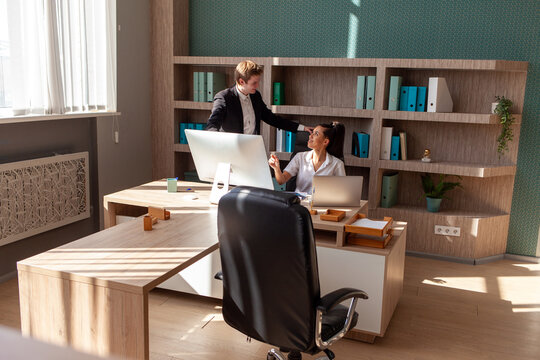 African American woman and European young man in business suit using computer and talking in office, office workers and business people at business meeting analyzing online statistics
