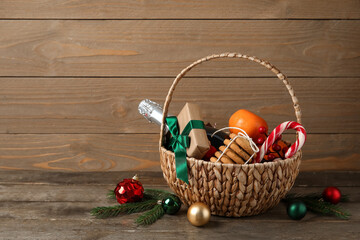 Gift basket with products, bottle of champagne and Christmas decor on wooden table