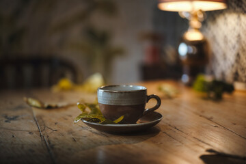 Warm Beverage Moment: Rustic Wooden Table, Ceramic Cup with Saucer, Autumn Leaves, and Soft Indoor Lighting. Perfect for Coffee, Tea, or Cozy Reflections.
