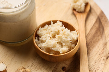 Bowl with horseradish sauce on wooden tray as background, closeup