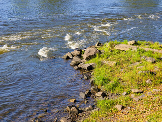Lakeside Landscape with Sparkling Blue Water, Green Grass and Rocks – Nature Background for Editorial and Commercial Use. Ultra High Resolution