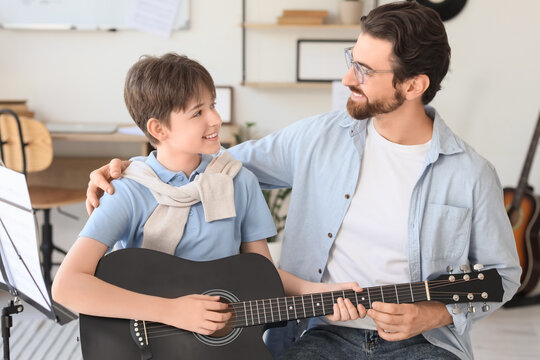 Cute boy learning guitar with private music teacher in room