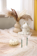 Glasses with autumn decor on dining table in room, closeup