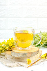 Glass cup of mullein herbal tea on natural wooden background with fresh Verbascum thapsus flowers
