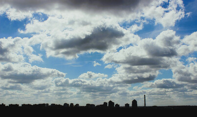 Dark silhouettes of high rise buildings and chimneys of city blocks under a contrasting cloudy sky  
