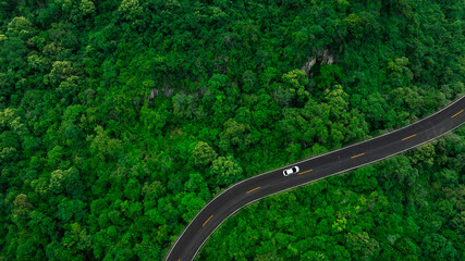 Aerial view of dark green forest road and white electric car Natural landscape and elevated roads Adventure travel and transportation and environmental protection concept	