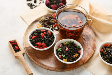 Bowls with different fruit tea and cup of brewed beverage on light background