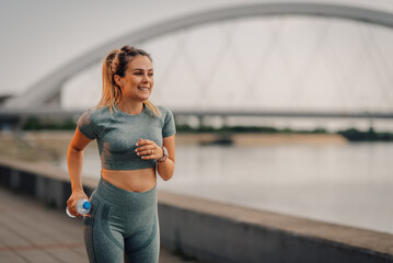 Young sporty woman running near river under bridge