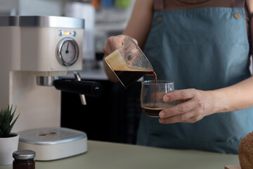 Woman is pouring brewed coffee into a glass