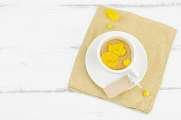 Cup of herbal tea with mullein flowers and leaves on neutral wooden background. Natural light