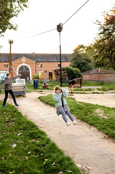 Cheerful girl swinging on zip line on playground.
