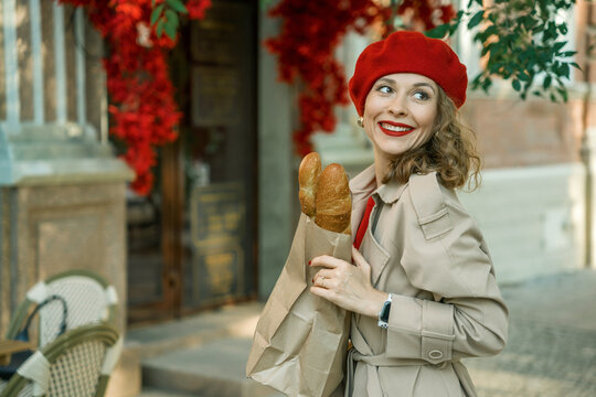 A stylish woman in a beige raincoat and a red beret with baguettes - Powered by Adobe